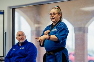 Close up of Shihan Carolyn as she speaks to students off camera. Grandmaster is seated to her left.