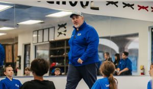 Grandmaster Steve Del Castillo teaching a group of students sitting on the blue mat in a martial arts dojo.