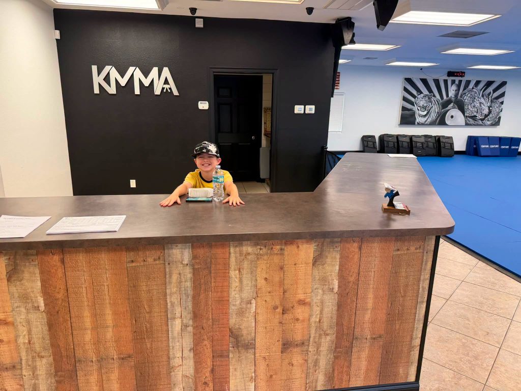 KMMA front desk area featuring a young smiling receptionist at the martial arts studio reception counter.