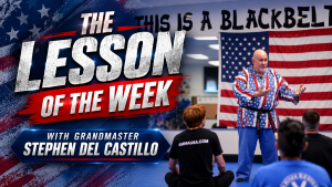 Promotional graphic titled "The Lesson of the Week with Grandmaster Stephen Del Castillo." Grandmaster Del Castillo, wearing a distinctive red, white, and blue patriotic-patterned martial arts uniform and black belt, stands instructing a class inside a dojo with an American flag hanging in the background. Several students are seated on the blue mat facing him.