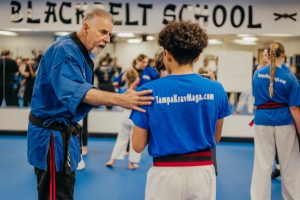 An experienced martial arts instructor places a guiding hand on a student’s shoulder while providing instruction in a dojo.