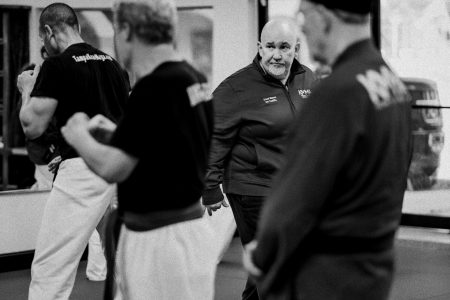 Black and white photo of Grandmaster Del Castillo looking serious while observing students as he walks the floor in his Dojo