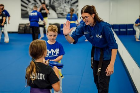 Sensei Mackenzie high-fives a student on the mat in the dojo