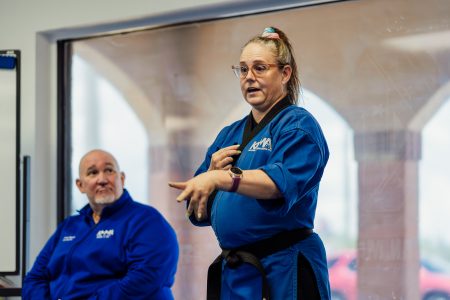 Close up of Shihan Carolyn as she speaks to students off camera. Grandmaster is seated to her left.