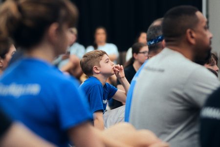 Young boy looks on in a crowd of students that are seated on the floor.